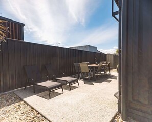Eine Terrasses mit Tisch und Stühlen, einem Holzzaun und blauem Himmel.