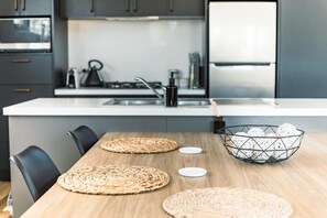 A modern kitchen with a wooden dining table, woven placemats, and a decorative basket. - Villa Callista - Modern Coastal Escape (Port Sorell)
