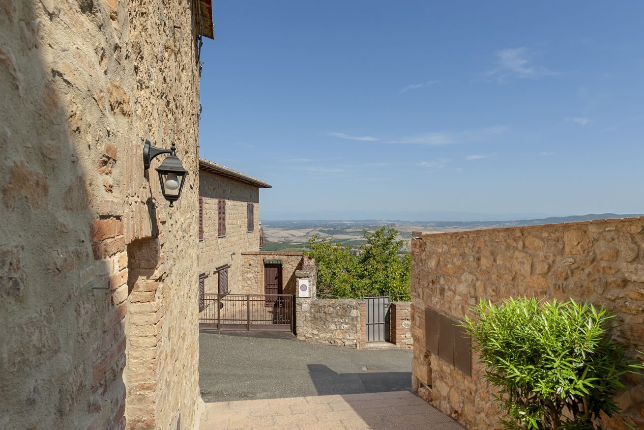 Un edificio in pietra con un cortile pavimentato, un cancello e vista sulla campagna.