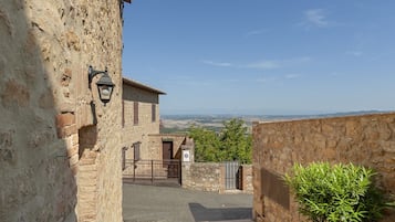 Un edificio in pietra con un cortile pavimentato, un cancello e vista sulla campagna.
