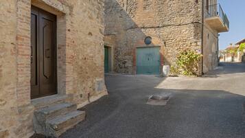 Eine enge Gasse mit Steinbauten, einer Metalttür und einem kleinen Podest, das zu einem Hauseingang führt.