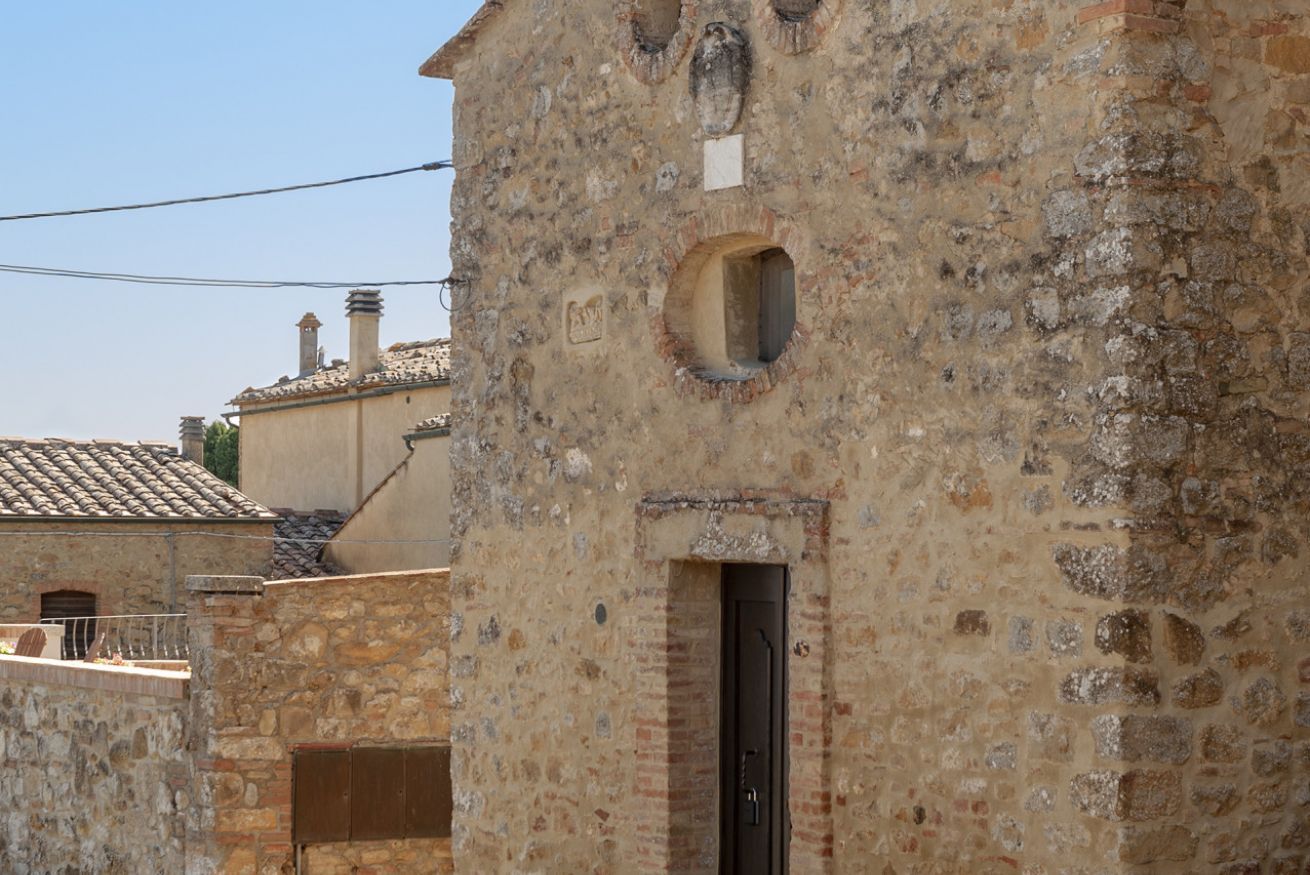Edifici de pedra amb una finestra circular i una porta, part d'una estructura més gran amb teulada d'aplaçament.