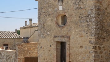Edifici de pedra amb una finestra circular i una porta, part d'una estructura més gran amb teulada d'aplaçament.