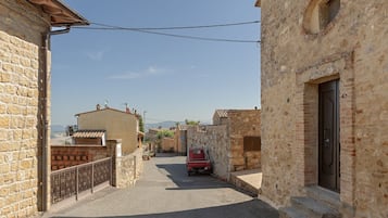 Un carrer estret amb edificis de pedra, un cotxe vermell aparcat al costat i un cel serè.