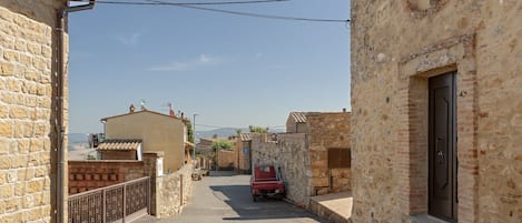 Una calle estrecha con edificios de piedra, un coche rojo estacionado al lado y un cielo despejado.