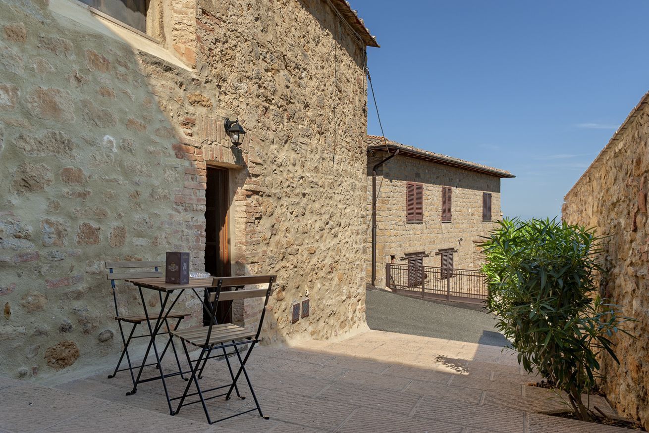 Edifici de pedra amb una petita zona d'seure a l'exterior i una taula de metall.