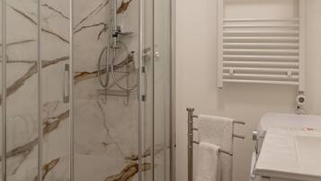 Un baño con cabina de ducha de vidrio, toallero y lavamanos blanco.