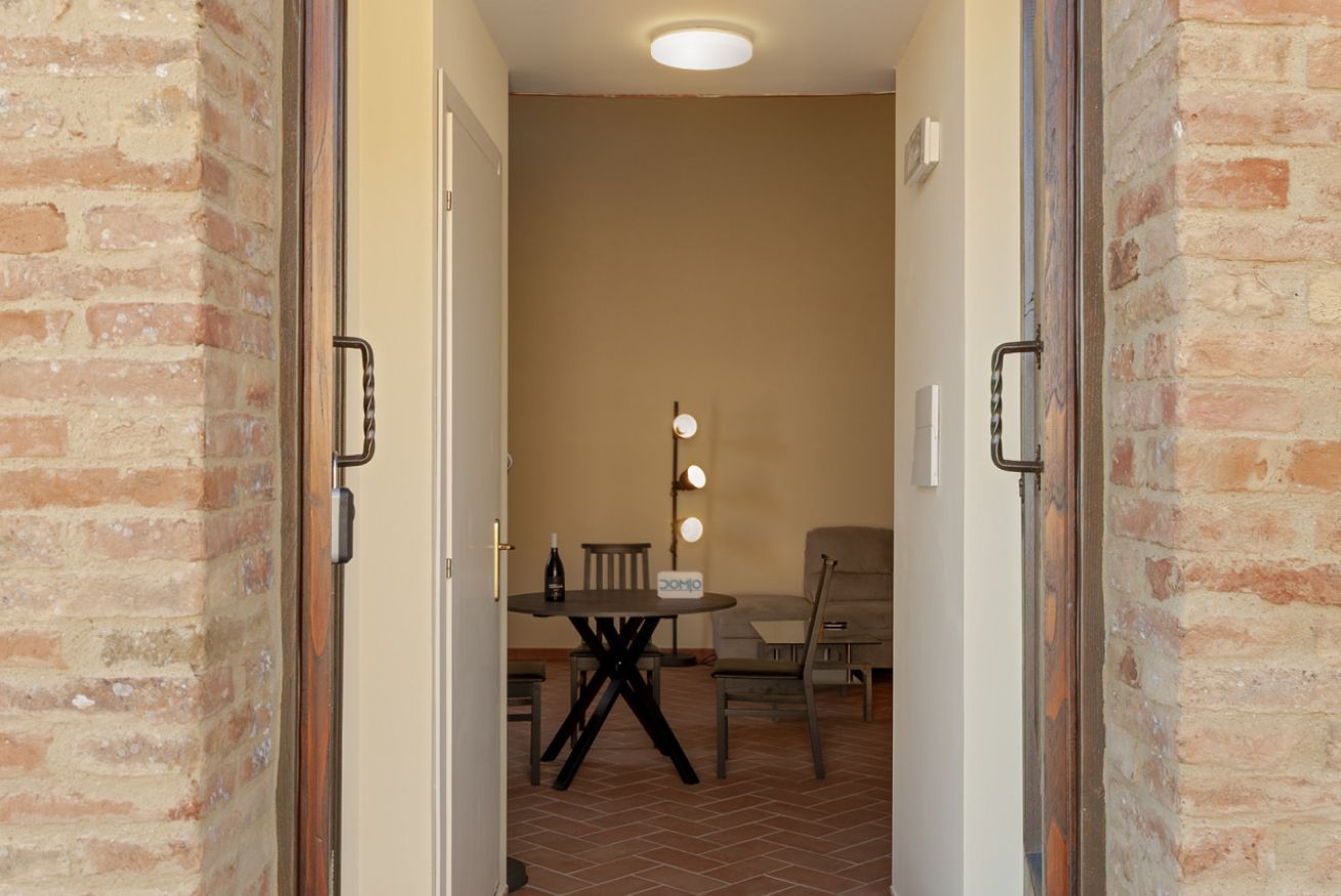 Una stanza con una parete in mattoni, un tavolo rotondo con sedie, un divano e una lampada fissata al muro.