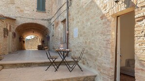 Kivinen rakennus, jonka kapea käytävä johtaa holvikaarelle. Ulkona on pieni oleskelualue, jossa on pöytä ja tuoleja.