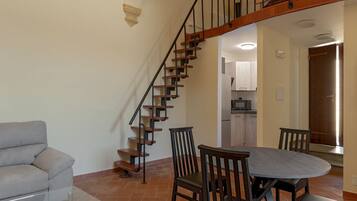 A living room with a sofa, a glass coffee table, a dining table with chairs, and a staircase with wooden steps and black railings.