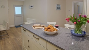 Uma cozinha com bancada de mármore, um recipiente com croissants, um vaso de tulipas e uma janela com vista.