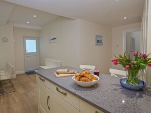 A kitchen with a marble countertop, a bowl of croissants, a vase of tulips, and a window with a view. - 4 The Salcombe (Salcombe)
