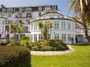A multi-story building with balconies, a curved section, and a well-maintained garden with palm trees. - 4 The Salcombe (Salcombe)