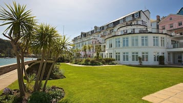 A coastal hotel with a well-maintained lawn, palm trees, and a view of the sea.