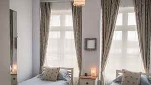 Quarto com duas camas de solteiro, mesa de cabeceira com abajur, espelho na parede e janela com cortinas.
