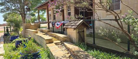 A stone building with a wooden staircase leading to a covered area, surrounded by potted plants and a flag.