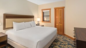 A hotel room with a large bed, a nightstand, a lamp, a mirror, and a wardrobe.