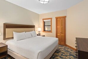 A hotel room with a large bed, a nightstand, a lamp, a mirror, and a wardrobe.