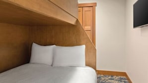 A bedroom with a bed, a wooden headboard, a flat-screen TV, and a door in the background.