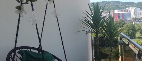A balcony with a hanging plant, a swing chair, and a view of the cityscape.