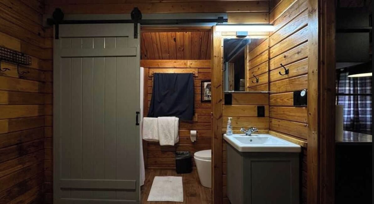 A wooden cabin bathroom with a toilet, sink, and a towel rack.