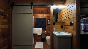 A wooden cabin bathroom with a toilet, sink, and a towel rack.