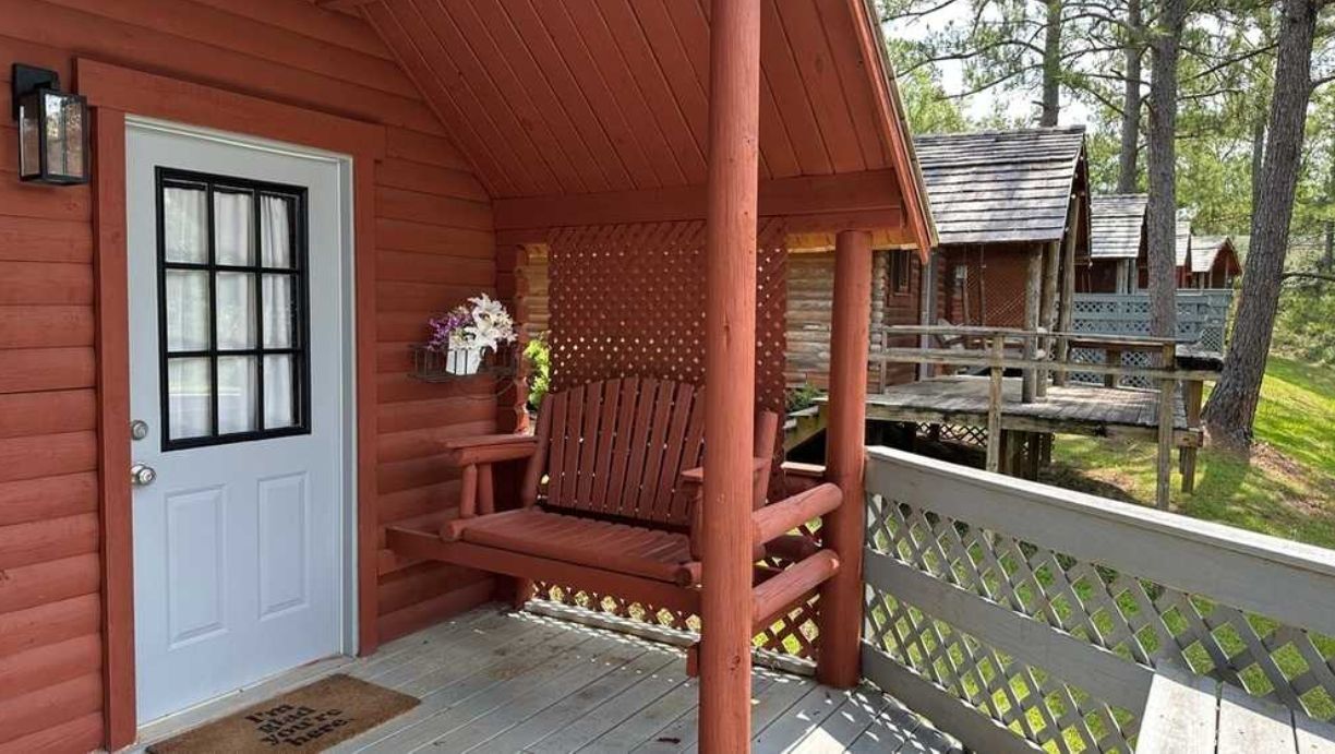 Une véranda en bois avec un banc, une porte et un petit espace jardin agrémenté de fleurs.