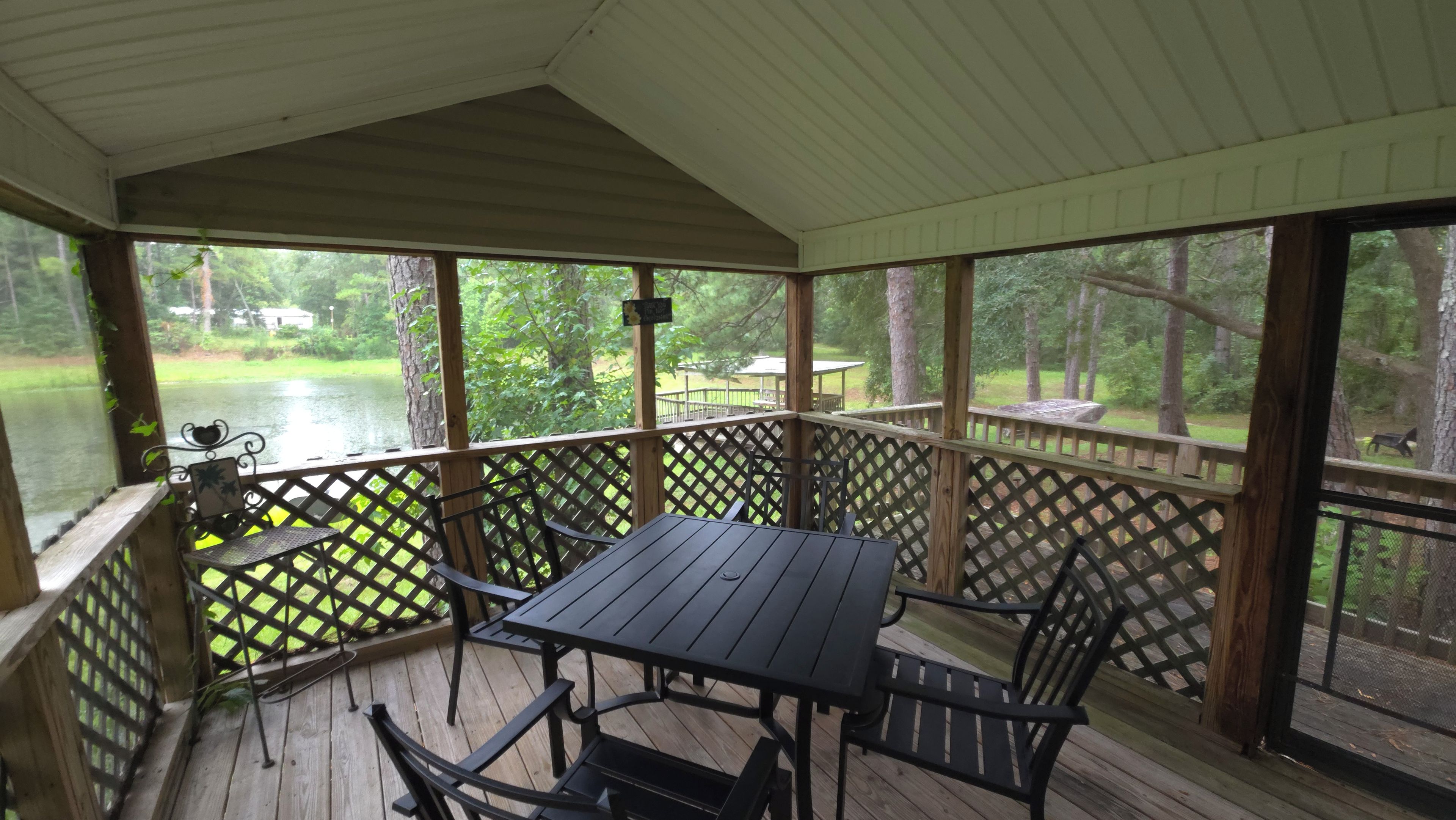 A covered outdoor deck with a table and chairs, overlooking a body of water and a grassy area.