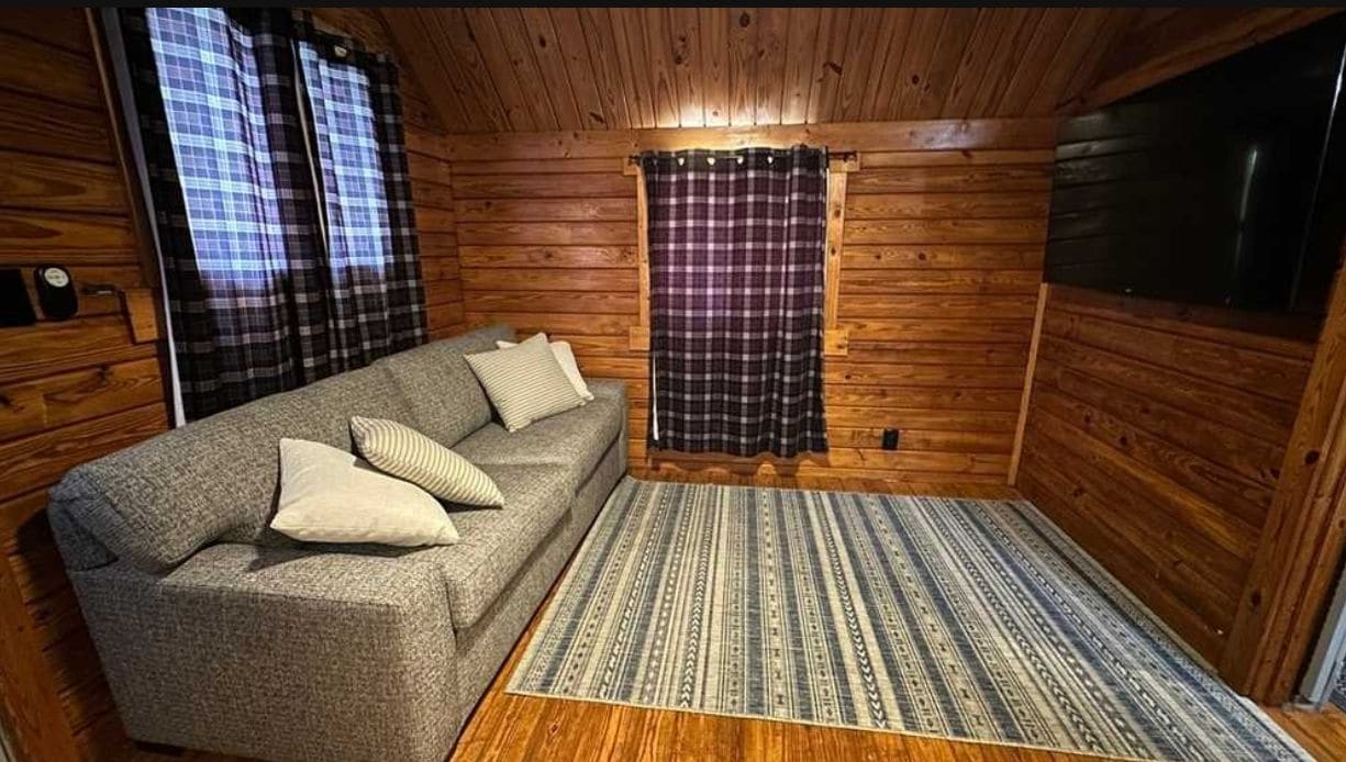 A log cabin interior with a sofa, patterned rug, and plaid curtains.
