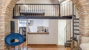 A loft-style room with a kitchen area, a dining table, and a blue chair. - Elegant Imperial Roman Apartment Near the Colosseum (Roma)