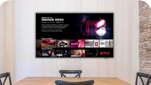 A wall-mounted display featuring a Netflix original series, surrounded by a dining area with a wooden table and black chairs. - Elegant Imperial Roman Apartment Near the Colosseum (Roma)