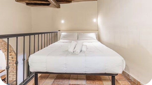 A bedroom with a bed, white linens, a wooden ceiling, and a brick wall. - Elegant Imperial Roman Apartment Near the Colosseum (Roma)