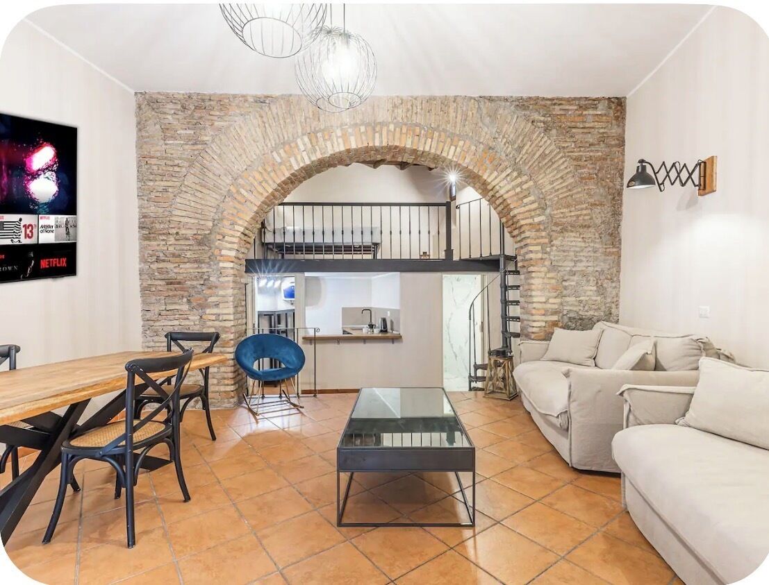 A living room with a stone archway, a sofa, a coffee table, and a TV mounted on the wall.