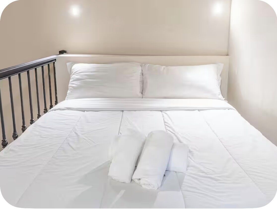 Ein ordentlich bezogenes Bett mit weißen Leinen und Kissen, ein schwarzes Metall-Kopfteil und eine weiße Wand.