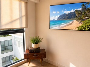A room with a window overlooking a beach, a potted plant, and a vintage suitcase on a small table. - Deluxe Retreat Steps from Larcomar (Miraflores)
