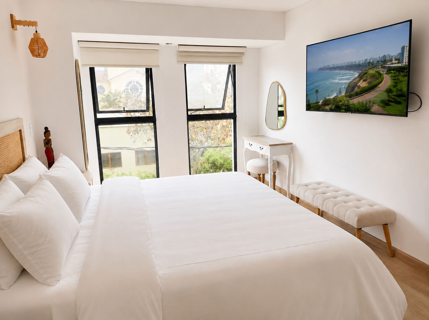 Quarto com uma cama grande, uma mesa de cabeceira, um banquinho, um espelho e uma janela com vista para a paisagem costeira.