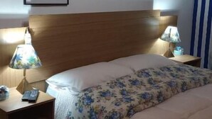 Ein Schlafzimmer mit einem hölzernen Kopfteil, zwei Nachttischlampen, einem Bett mit blumigem Überwurf und zwei gerahmten Bildern an der Wand.