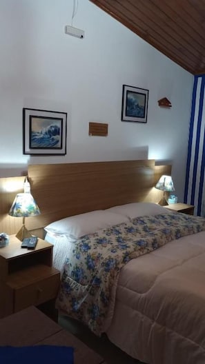 A bedroom with a wooden headboard, two bedside lamps, a bed with a floral bedspread, and two framed pictures on the wall. - Rancho da raposa (Campos do Jordão)