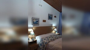 Ein Schlafzimmer mit einem Holzkopfteil, einem Bett mit floralem Überwurf, zwei Nachttischlampen und einem Nachttisch.