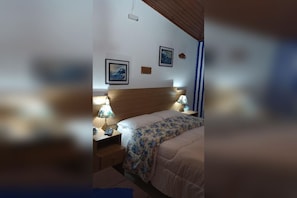A bedroom with a wooden headboard, a bed with a floral bedspread, two bedside lamps, and a nightstand. - Rancho da raposa (Campos do Jordão)