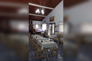 A dining area with multiple tables and chairs, a wooden ceiling, and a television screen. - Rancho da raposa (Campos do Jordão)
