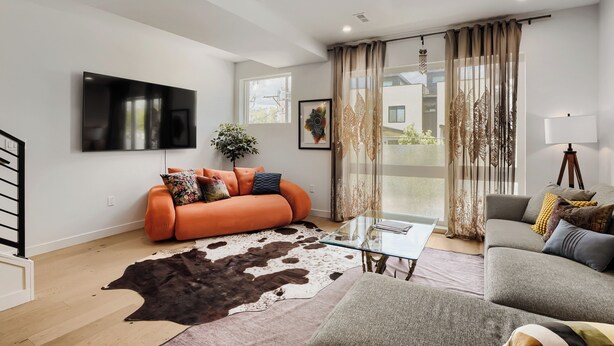 A modern living room with a sofa, a glass coffee table, a mounted TV, and a large window with curtains. - 3BR/3.5BA Rooftop Home + Private Flat | Tennyson (Denver)