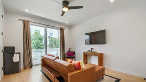 A modern living room with a sofa, a flat-screen TV, a ceiling fan, and a sliding glass door leading to an outdoor area. - 3BR/3.5BA Rooftop Home + Private Flat | Tennyson (Denver)