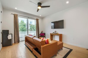 A modern living room with a sofa, a flat-screen TV, a ceiling fan, and a sliding glass door leading to an outdoor area. - 3BR/3.5BA Rooftop Home + Private Flat | Tennyson (Denver)