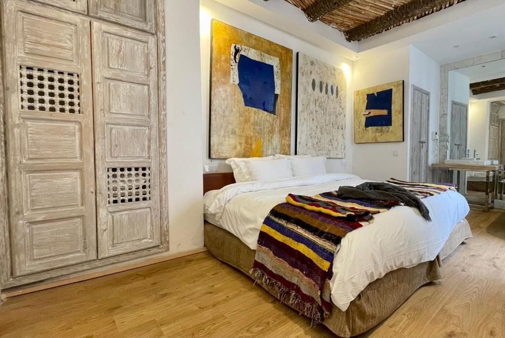 A bedroom with a large bed, a wardrobe, and artwork on the walls.