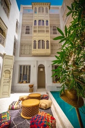Un patio con piscina, cojines tradicionales y un edificio con ventanales de arco.