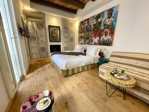 Un dormitorio con una cama, una mesita con un plato, una mesita auxiliar de fibras naturales y una pared con un mural colorido.