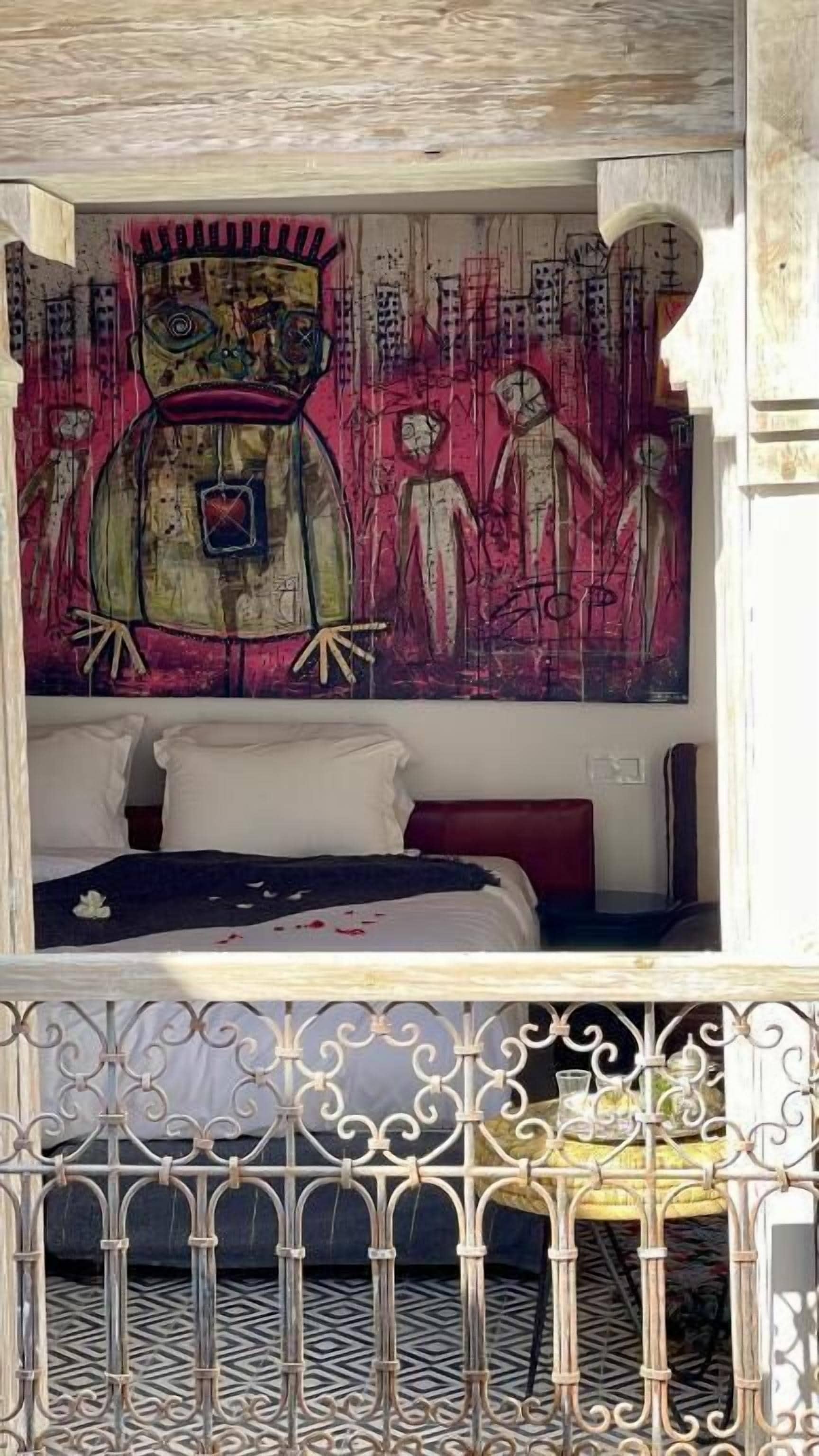 A room with a bed, a wall with abstract art, and a balcony with a wrought iron railing.