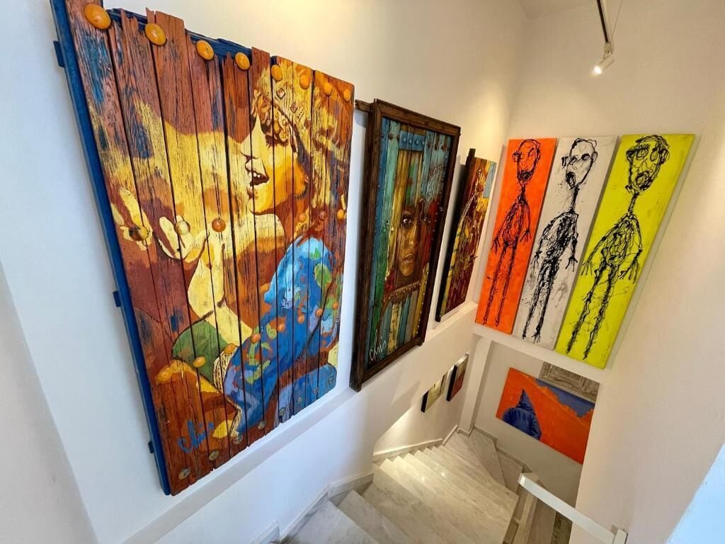 A staircase with a handrail and steps, leading to a landing where artworks are displayed on the wall.