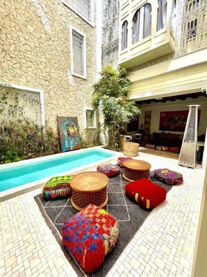 A courtyard with a pool, outdoor seating, and a stone wall. - BCK Art Riad (Marrakech)